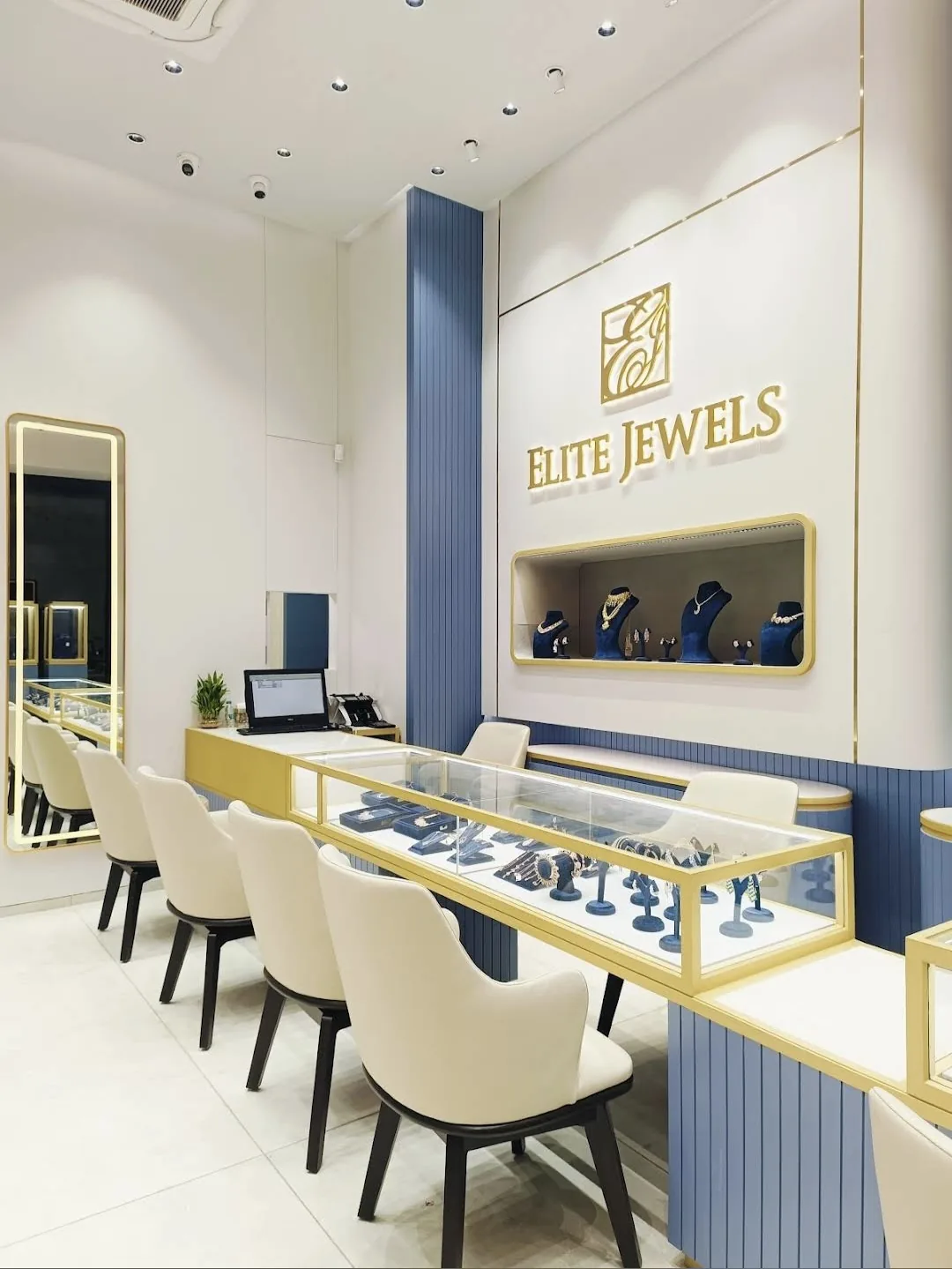 Showroom counter with cream chairs and a wall niche of necklaces under the Elite Jewels logo