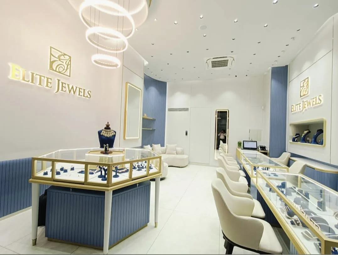 Inside the Elite Jewels showroom in Surat: gold-framed display cases, a polki necklace on a blue bust and seating along the counters